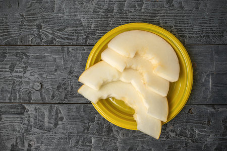 Sliced Melon on Yellow Plate with Rustic Wooden Backgroundの写真素材