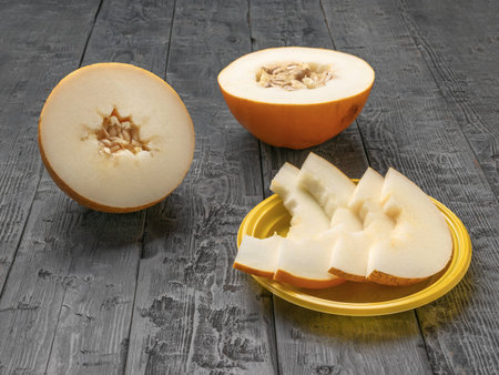 Fresh Sliced Melon on Yellow Plate and Whole Melon on Rustic Wooden Tableの写真素材