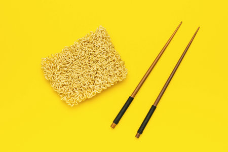 Instant Noodles with Wooden Chopsticks on Vibrant Yellow Background - Minimalistic Food Photographyの写真素材