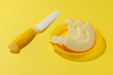 Sliced Melon with Knife on Bright Yellow Background - Fresh Summer Fruitの写真素材