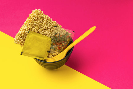 Instant Ramen Noodles and Seasoning in Bowl with Fork on Pink and Yellow Backgroundの写真素材