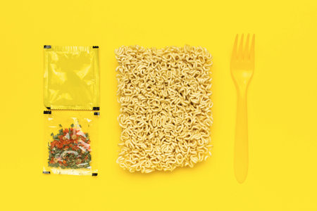 Instant Noodles with Seasoning Packets and Fork on Bright Yellow Backgroundの写真素材