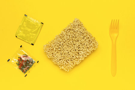 Instant Noodles and Seasoning Packets with Yellow Fork on Vibrant Yellow Backgroundの写真素材