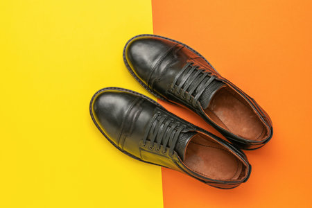 Stylish Black Leather Men's Shoes on Vibrant Yellow and Orange Backgroundの写真素材