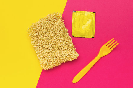 Dry noodles, a yellow fork and a bag of spices on a red and yellow background.の写真素材
