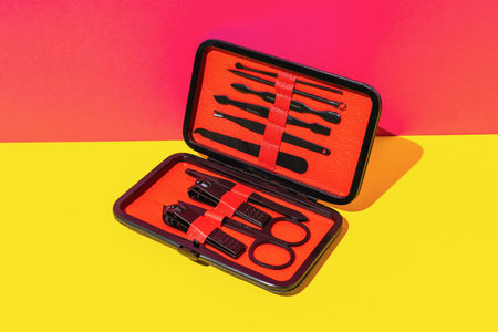 Stylish Black Manicure Set in Orange Case on Vibrant Yellow and Red Backgroundの写真素材