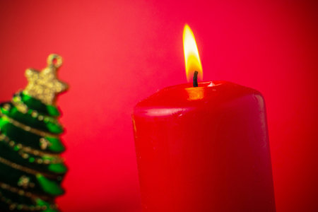 Red Candle and Christmas Tree Ornament against Red Background - Festive Holiday Decorationの写真素材