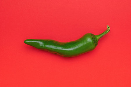Fresh Green Chili Pepper on Vibrant Red Background Minimalist Food Photographyの写真素材