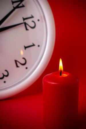 Lit Red Candle and Clock on Red Background Representing Time and Reflectionの写真素材