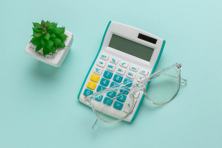 Office Desk Essentials with Calculator, Glasses, and Small Succulent on Light Blue Backgroundの写真素材