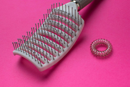 Hairbrush and Clear Spiral Hair Tie on Vibrant Pink Background - Beauty and Fashion Accessoriesの写真素材