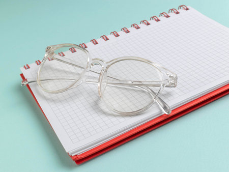 Clear Eyeglasses Resting on Red Spiral Notebook with Graph Paper on Green Backgroundの写真素材