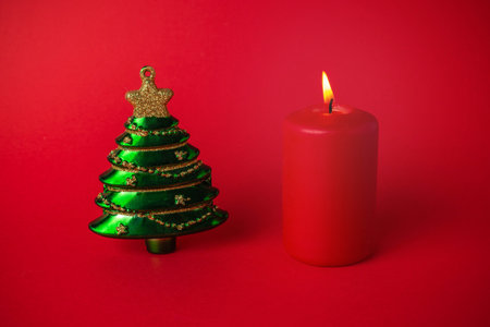 Festive Green Christmas Tree Ornament and Red Candle Against Vibrant Red Backgroundの写真素材