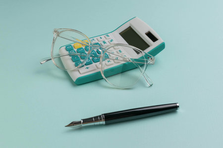 Clear Glasses, White Calculator, and Fountain Pen on Light Green Background - Office Essentials Conceptの写真素材