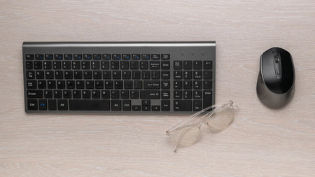 Wireless Keyboard and Mouse with Glasses on Wooden Desk for Modern Office Setupの写真素材