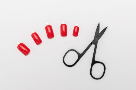Set of Red False Nails and Black Scissors on White Background