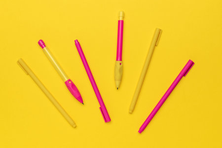 Bright Yellow and Pink Pens Arranged on Vibrant Yellow Background for Creative Stationery Designの写真素材
