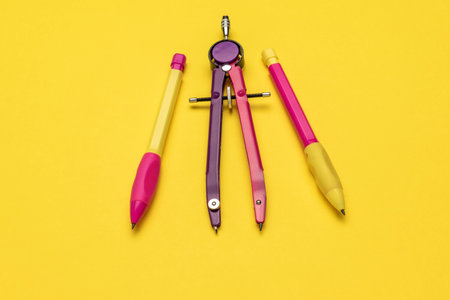 Colorful Stationery Trio: Compass, Yellow and Pink Pencils on Vibrant Yellow Backgroundの写真素材