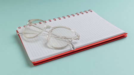 Clear Glasses on Red Spiral Notebook with Graph Paper Against Light Blue Backgroundの写真素材