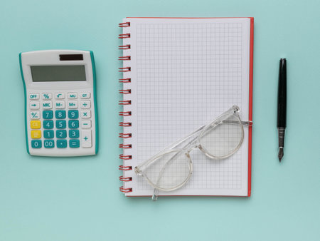 Office Supplies: Calculator, Glasses, Grid Notebook, and Pen on Pastel Backgroundの写真素材