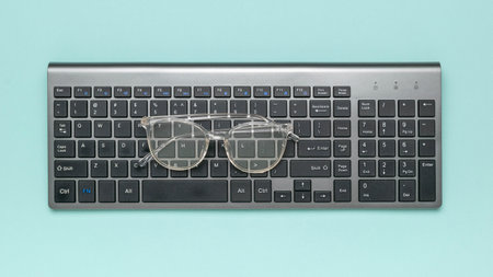 Eyeglasses on Wireless Keyboard Against Pastel Background: Modern Office Essentialsの写真素材