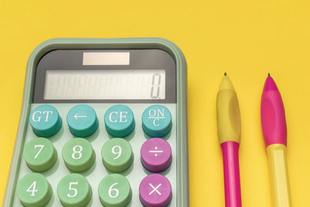 Colorful Calculator with Multicolored Buttons and Pens on Yellow Backgroundの写真素材