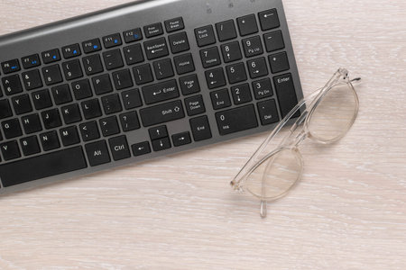 Black Keyboard and Round Glasses on Light Wooden Desk - Office Work Workspace Essentialsの写真素材