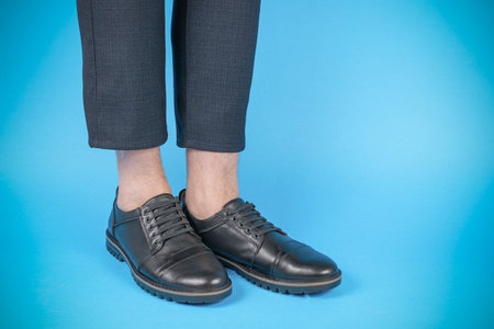 Close-up of Stylish Black Leather Shoes with Business Casual Pants on Blue Backgroundの写真素材