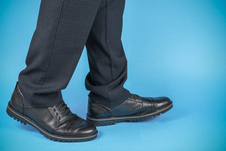 Businessman's Formal Shoes and Dark Gray Trousers Against Blue Backgroundの写真素材