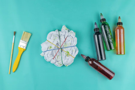 Tie-Dye T-Shirt Creation with Brushes and Colorful Dye Bottles on Teal Backgroundの写真素材