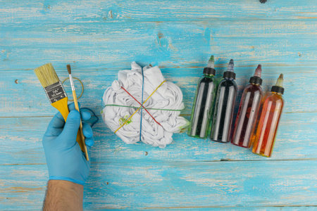 DIY Tie-Dye Crafting with Tied Shirt, Dye Bottles, and Paintbrush on a Wooden Surfaceの写真素材