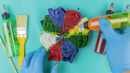 Hands Dyeing Fabric with Colorful Tie-Dye Technique on Turquoise Backgroundの写真素材