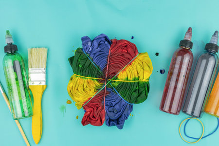 Vibrant Tie-Dye Shirt with Paint Bottles and Brush on Aqua Backgroundの写真素材