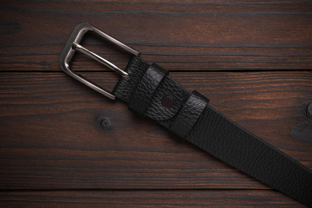 Black Leather Belt with Metal Buckle on Dark Wooden Surface - Rustic Fashion Accessoryの写真素材