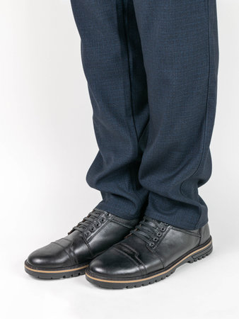 Close-Up of Black Leather Shoes and Blue Trousers on White Backgroundの写真素材