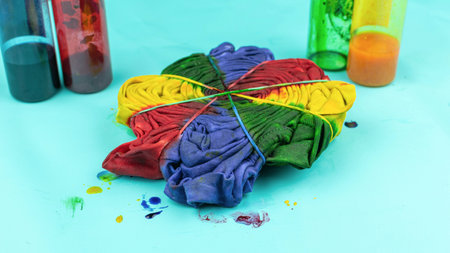 Colorful Tie-Dye Fabric with Bands Surrounded by Dye Bottles on Blue Backgroundの写真素材