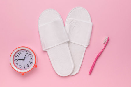 Morning Essentials: White Slippers, Alarm Clock, and Pink Toothbrush on Pastel Pink Backgroundの写真素材