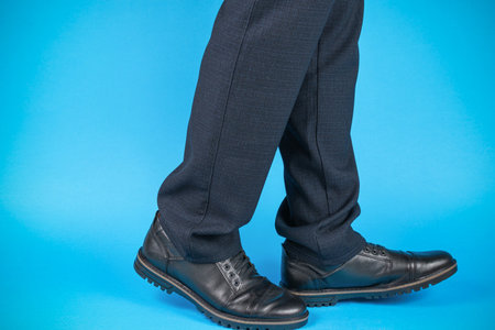 Stylish Businessman in Dark Trousers and Black Shoes Against Blue Backgroundの写真素材
