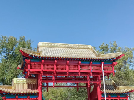 Traditional Red Pagoda Gate with Golden Roof Under Clear Blue Sky and Greeneryの写真素材