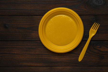 Yellow Plastic Plate and Fork on Dark Wooden Surface - Minimalist Table Settingの写真素材