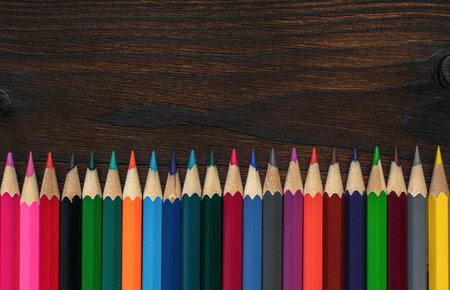 Colorful Pencils Aligned in Row on Dark Wooden Background in Creative Art Compositionの写真素材