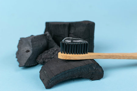 Bamboo Toothbrush with Charcoal Toothpaste on Charcoal Pieces Against Blue Background