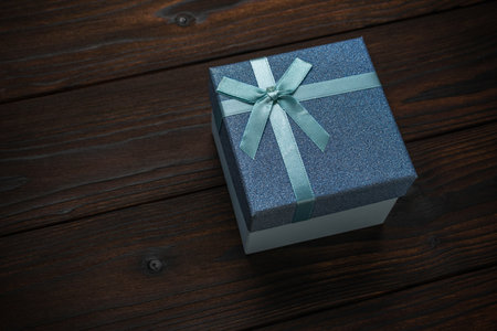 Blue Gift Box with Light Blue Ribbon on Dark Wood Background - Elegant Present for Special Occasionsの写真素材
