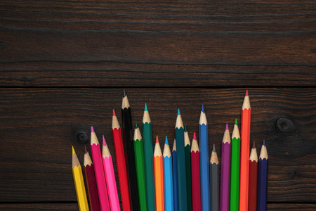 Assorted Colored Pencils Arranged on Dark Wooden Surface for Art and Drawingの写真素材