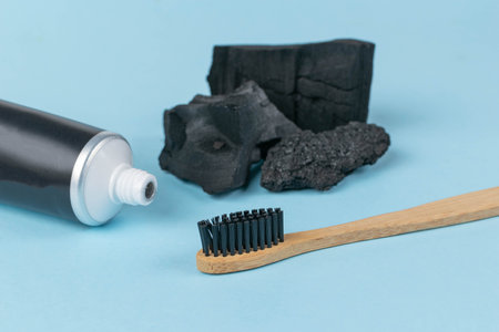 Charcoal Toothpaste and Bamboo Toothbrush with Activated Charcoal Pieces on Blue Backgroundの写真素材