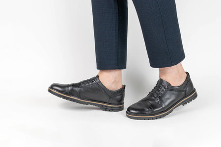 Close-up of Stylish Black Leather Shoes with Navy Blue Pants on White Backgroundの写真素材