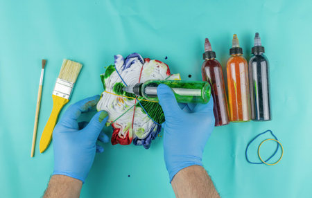 Colorful Tie-Dye Creation Process with Bottles and Brushes on Aqua Backgroundの写真素材