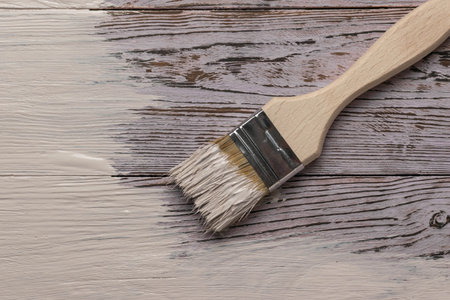 Close-Up of Paintbrush Applying White Paint on Rustic Wooden Surfaceの写真素材