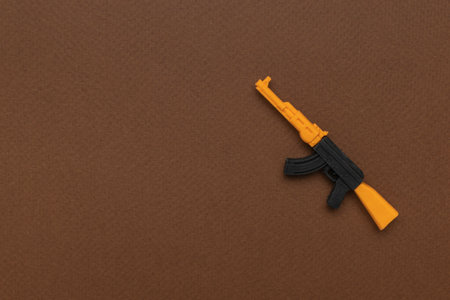 Minimalist Orange and Black Toy Rifle on Brown Background Representing Childhood and Imaginationの写真素材