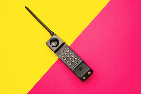 Retro Mobile Phone on Vibrant Yellow and Pink Diagonal Backgroundの写真素材